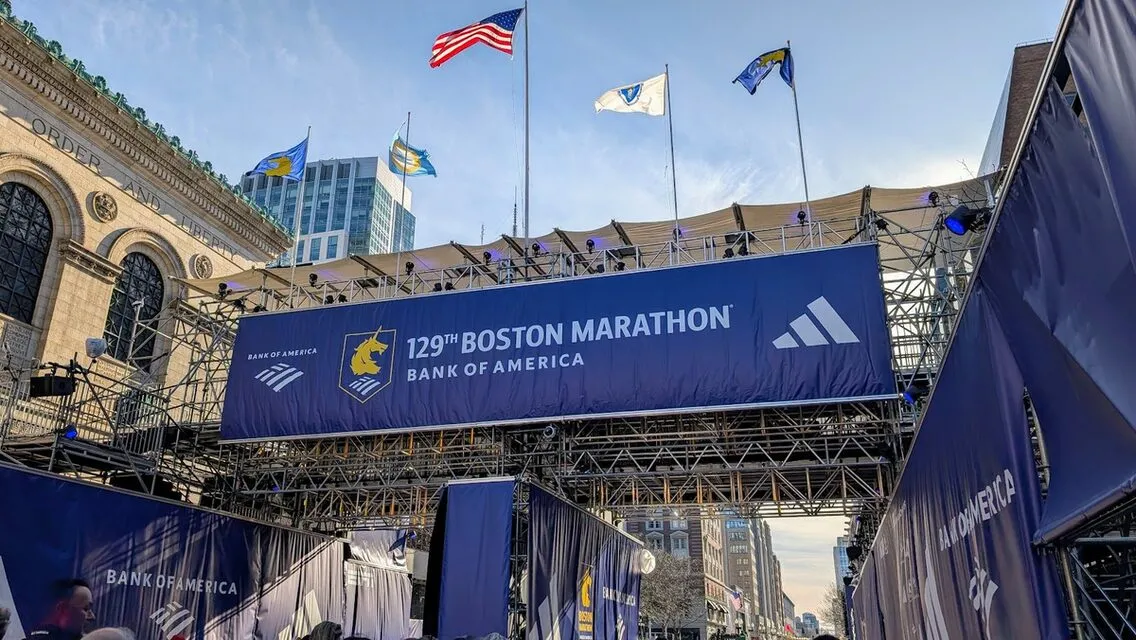 The blue Boston Marathon finish-line gantry over Boylston Street by the Boston Public Library, with flags above