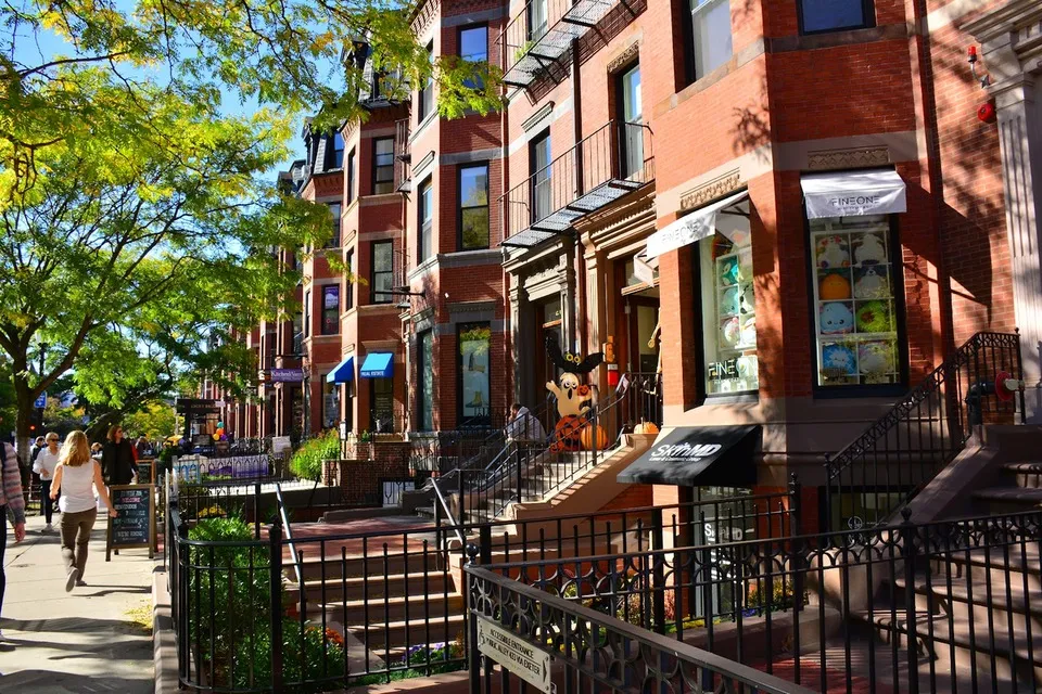 Brownstone shops with bay windows and awnings along leafy Newbury Street